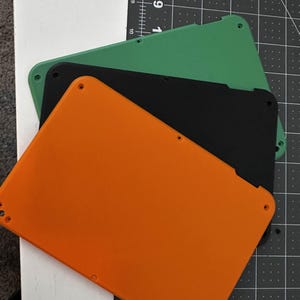 May include: Three plastic plates in orange, black, and green. The plates are stacked on top of each other.
