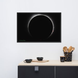 Può includere: Stampa incorniciata di un'eclissi solare, che mostra un disco nero circondato da una corona luminosa. L'immagine è ambientata su uno sfondo scuro, con un sottile bordo bianco. La cornice è nera. La stampa è esposta su una parete bianca.