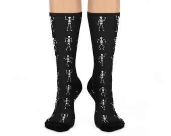 May include: A pair of black crew-length socks featuring a repeating white graphic pattern of dancing skeletons in various poses. The skeletons are depicted in a simple line-art style, distributed evenly across the dark fabric of the socks.