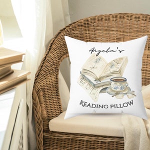 May include: White pillow with a watercolor illustration of an open book, a cup of coffee, and the text "Angela's Reading Pillow".
