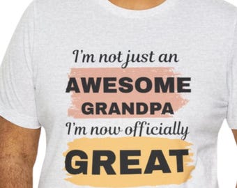 May include: Light gray t-shirt with the text "I'm not just an AWESOME GRANDPA I'm now officially GREAT EST. 2025" in black, with orange and pink accents. The shirt is a crew neck style.