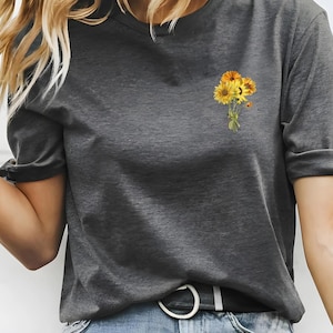May include: A grey t-shirt with a small bouquet of yellow sunflowers printed on the left side of the chest.
