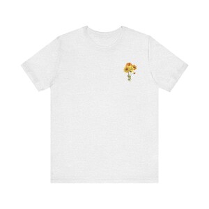 May include: A heather grey t-shirt with a small bouquet of yellow and orange flowers printed on the left chest.