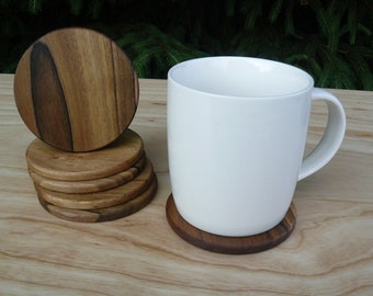 May include: A set of six round wooden coasters with a natural wood grain finish. The coasters are stacked on top of each other. A white ceramic mug is sitting on a single coaster.