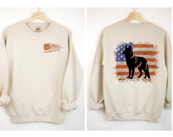 May include: A beige sweatshirt with a distressed American flag design on the left chest and a silhouette of a German Shepherd dog standing in front of a distressed American flag on the back.