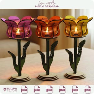 May include: Three laser-cut tulip candle holders in shades of pink, orange, and yellow. Each tulip has a small candle inside, casting a warm glow. The holders are on black stems with leaf details and wooden bases. The text "laser cut file DIGITAL DOWNLOAD" is at the top.
