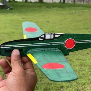 May include: A green and red wooden model airplane with a yellow propeller. The airplane has Japanese markings, including a red circle with a white dot on the wings and a red tail with a white lightning bolt.