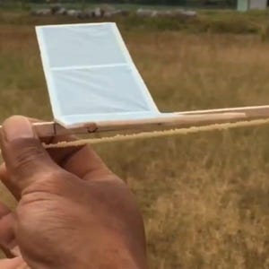 May include: A wooden toy aeroplane with a propeller and a clear plastic wing. The aeroplane is held in a person's hand.