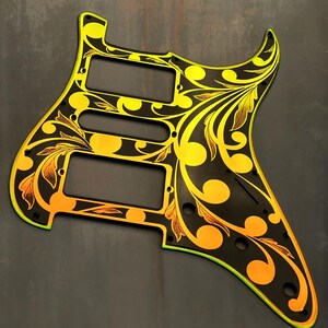 May include: A black guitar pickguard with a gold and yellow floral design. The pickguard has a  "DUSTSTORM ENGRAVING" logo in the bottom left corner.