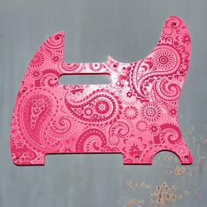 Op de afbeelding: Een roze gitaar pickguard met een paisley-patroon. De pickguard is gemaakt van plastic en heeft een glanzende afwerking.