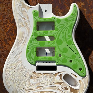 Op de afbeelding: Een witte elektrische gitaar body met een groen bloemenpatroon en een wit bloemenontwerp op de onderste body. De gitaar body is gegraveerd met de tekst "DUSTSTORM ENGRAVING".