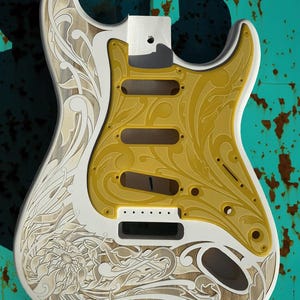 May include: White electric guitar body with a yellow and white floral design. The design is engraved into the wood. The guitar body is blank, with no pickups or other hardware installed. The text "DUSTSTORM ENGRAVINGS" is visible in the upper right corner of the image.