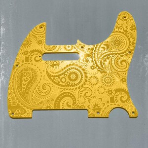 Op de afbeelding: Een goudkleurige gitaar pickguard met een gedetailleerd paisley patroon. De pickguard heeft een unieke vorm met verschillende schroefgaten en een uitsparing voor de pickups van de gitaar. De tekst "DUST STORM ENGRAVING" staat onderaan.