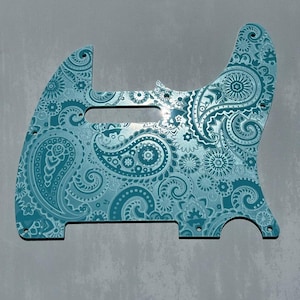 Op de afbeelding: Een turquoise gitaar pickguard met paisley patroon. De pickguard heeft een gedetailleerd ontwerp van wervelende paisley vormen en bloemelementen. De tekst "DUST STORM ENGRAVING" staat onderaan.