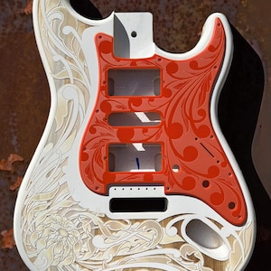 May include: A white electric guitar body with a red pickguard. The guitar body is decorated with an intricate floral design carved into the wood. The text "DUSTSTORM ENGRAVING" is visible at the top of the image.