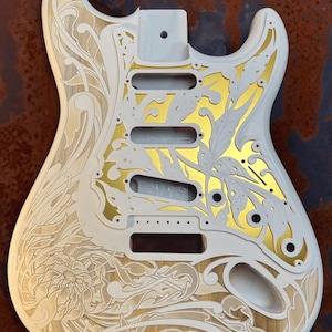 May include: White electric guitar body with a gold leaf floral design and the text "DUSTSTORM ENGRAVING" in the top right corner.