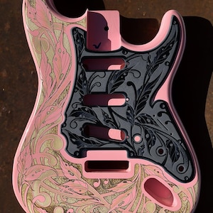 May include: A pink electric guitar body with a black and gold floral design. The guitar is engraved with the text "DUSTSTORM ENGRAVING".