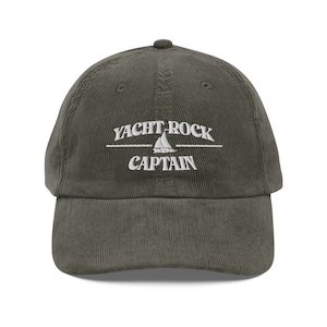 May include: A dark green corduroy baseball cap with white embroidery that reads "YACHT ROCK CAPTAIN" and features a sailboat graphic.