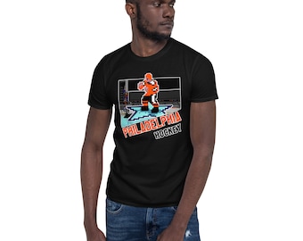 Puede incluir: Camiseta negra con una imagen pixelada de un jugador de hockey en una pista de hielo azul y blanca. El texto "PHILADELPHIA HOCKEY" está impreso debajo de la imagen.