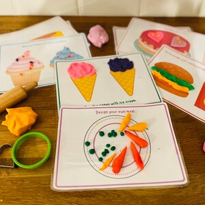 May include: A set of printable cards featuring different food items, such as cupcakes, ice cream cones, burgers, and french fries. The cards are designed for use with play dough, and there are several pieces of play dough in different colors, as well as a rolling pin and cookie cutters.