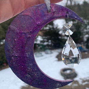 May include: A purple and silver glitter crescent moon ornament with a crystal prism hanging from it.