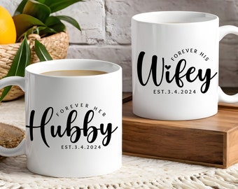May include: Two white ceramic mugs with black text. The mug on the left says "Forever Her Hubby Est. 3.4.2024". The mug on the right says "Forever His Wife Est. 3.4.2024".