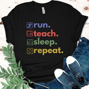 Puede incluir: Camiseta negra con un gráfico blanco que dice "run. teach. sleep. repeat."