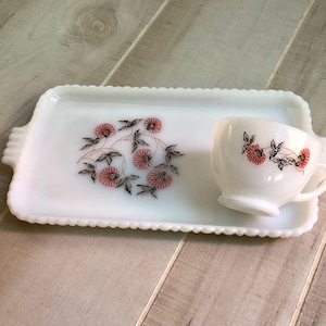 May include: White milk glass serving tray with a scalloped edge and a floral design in red and black. A matching white milk glass cup with a floral design in red and black is on the tray.