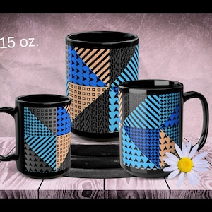 May include: Three black coffee mugs with geometric patterns in blue, tan, gray, and black. The largest mug is labeled "15 oz." The mugs are arranged on a wooden surface with a daisy.