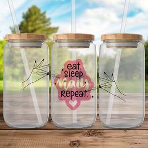 May include: Three clear glass tumblers with bamboo lids and straws. The middle tumbler has a pink and yellow graphic with the text "eat. sleep. nails. repeat." and a pink heart.