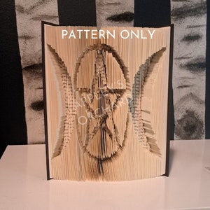 May include: A book art sculpture of a triple moon and pentacle symbol. The sculpture is made from a book with pages folded and cut to create the design. The sculpture is displayed on a white surface with a black and white striped background.