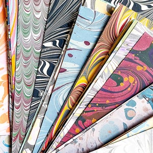May include: A collection of colorful marbled paper sheets in various patterns and colors, including blue, green, red, and yellow. The sheets are arranged in a fan shape, with the tips of the sheets pointing towards the center of the image.