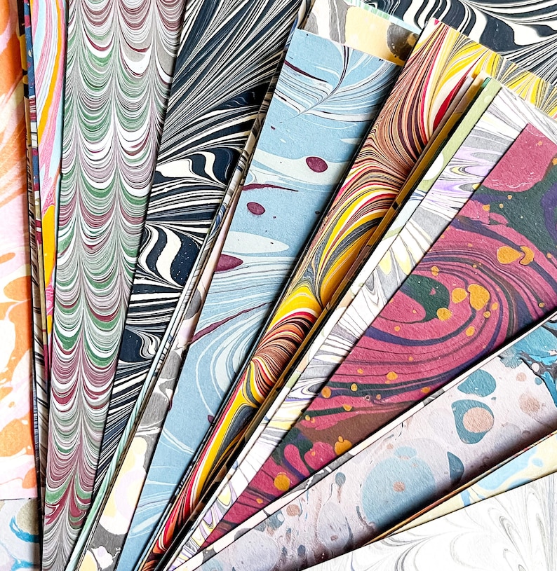 May include: A collection of colorful marbled paper sheets in various patterns and colors, including blue, green, red, and yellow. The sheets are arranged in a fan shape, with the tips of the sheets pointing towards the center of the image.