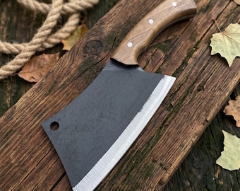 May include: A heavy-duty meat cleaver featuring a dark, matte-finished steel blade with a circular hole near the top corner and a polished, light brown wooden handle secured by three silver-toned metal rivets along the curved grip.
