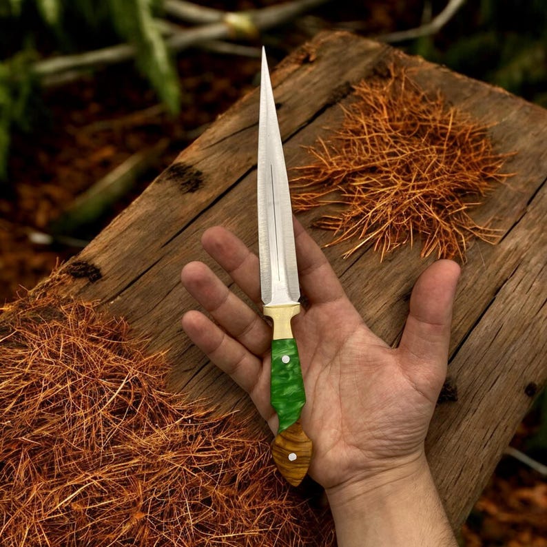 May include: A silver dagger with a green and brown handle. The dagger is resting on a wooden surface.