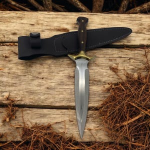 May include: A silver dagger with a gold-colored hilt and a black leather sheath. The dagger is lying on a wooden surface with brown twigs.