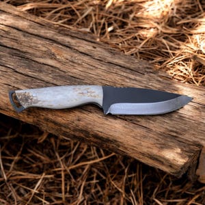 May include: A black-handled knife with a white bone handle and a black blade. The knife is lying on a piece of weathered wood.