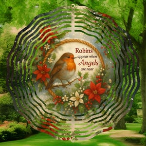 May include: A decorative metal wind spinner featuring a robin perched on a branch within a wreath of poinsettias and berries. The text reads "Robins appear when Angels are near". The outer frame has a wavy, layered design.