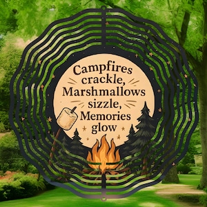 May include: Black metal wind chime with a circular design. The chime features a campfire scene with flames, trees, and a marshmallow on a stick. The text "Campfires crackle, Marshmallows sizzle, Memories glow" is written on the chime.