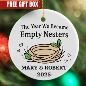 May include: White ceramic ornament with the text "The Year We Became Empty Nesters" and a nest illustration. Includes the names "MARY & ROBERT" and the year "-2025-". The ornament has a gold string for hanging.