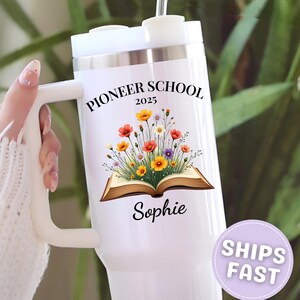 May include: White insulated tumbler with a handle, featuring the text "PIONEER SCHOOL 2025" and a floral design above the name "Sophie". The tumbler has a white lid and a straw.