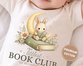 May include: A cream-colored baby bodysuit featuring a graphic of a bunny sitting on a book and a crescent moon, surrounded by flowers. The text reads, "the littlest BOOK CLUB member" and a circular badge states "PREMIUM COTTON" in white text.