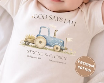 May include: Cream-colored baby onesie with a blue tractor illustration and the text "GOD SAYS I AM STRONG & CHOSEN." The onesie also has a "PREMIUM COTTON" label. The design features wheat and a white flag.