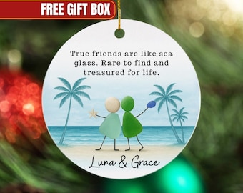 May include: A round, white ornament with a beach scene featuring two figures made of pebbles, holding a starfish and a blue object. Text reads "True friends are like sea glass. Rare to find and treasured for life." and "Luna & Grace."