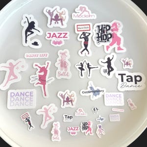 Puede incluir: Un conjunto de pegatinas con temática de baile en varios colores, incluyendo rosa, morado y negro. Las pegatinas presentan siluetas de bailarines, zapatillas de ballet y texto como "Jazz", "Hip Hop" y "Ballet".