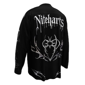 May include: Black long-sleeved shirt with the text "Niteharts" in a dripping font on the back. The shirt features a silver, stylized graphic design on the back and sleeves. The design has a gothic or edgy aesthetic.