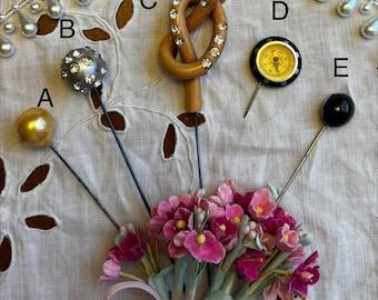 May include: A collection of five decorative lapel pins labeled A through E. Pin A has a gold sphere, B a silver sphere with rhinestones, C a tan knot with rhinestones, D a yellow compass, and E a black circular top. They are arranged together.