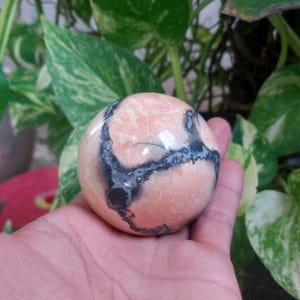May include: A smooth, round, pink and black sphere with a swirling pattern. The sphere is made of polished stone.