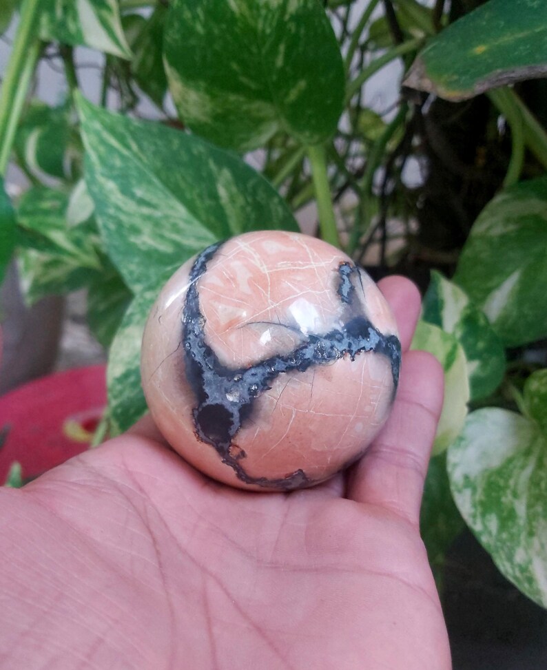 May include: A smooth, round, pink and black sphere with a swirling pattern. The sphere is made of polished stone.