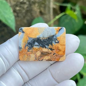 May include: A rectangular polished stone cabochon featuring a complex pattern of mustard yellow, charcoal gray, and white veins. The surface displays a natural, marbled texture with distinct color blocks and intricate, dark, jagged inclusions.